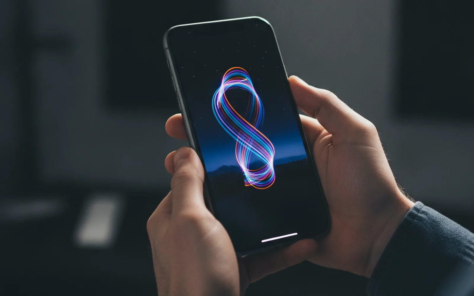 Разработчик держит iPhone с запущенным светящимся эффектом анимации в тёмной студии — тестирование творческого iOS-приложения
